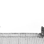 An artistic black and white image of a roof with a chimney and a tree, showcasing minimalist architecture.