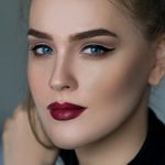 Close-up portrait of an elegant woman with striking makeup and blue eyes.