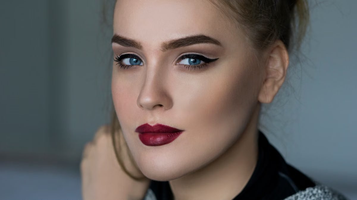 Close-up portrait of an elegant woman with striking makeup and blue eyes.