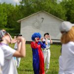 Group enjoying a clown performance in a sunny park setting. Perfect for summer festival themes.